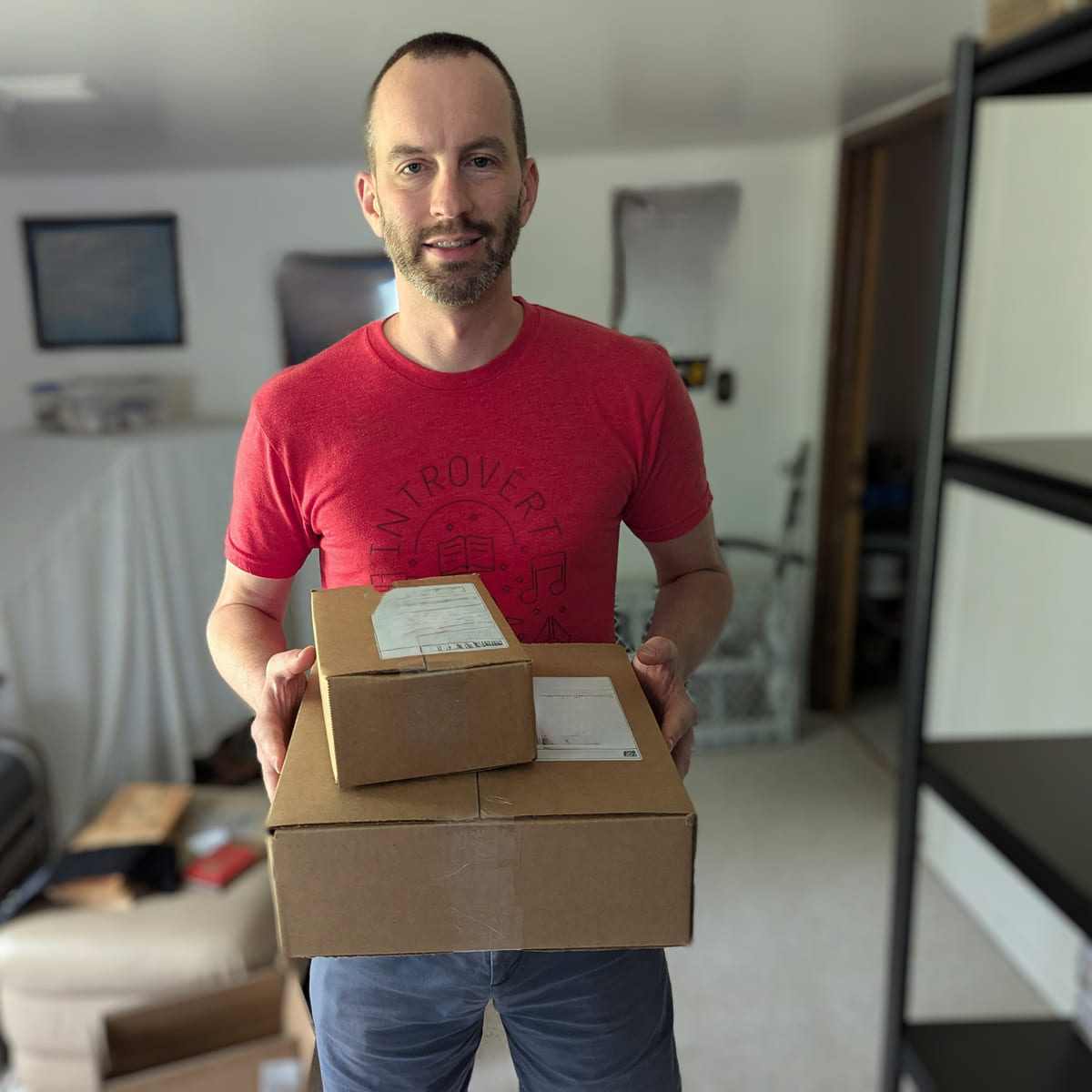 A Middle Mile team member holding two packed and labeled cartons in a home fulfillment space, with steel shelving behind them.